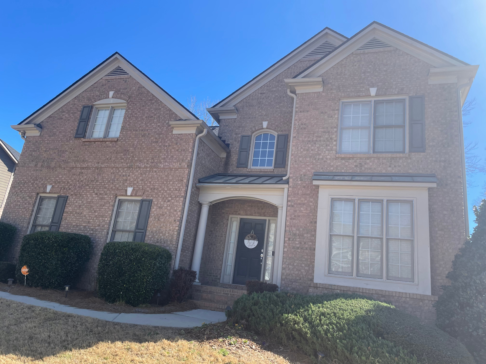 Two-story brick home with arched entry, columns, and standing-seam metal porch roof