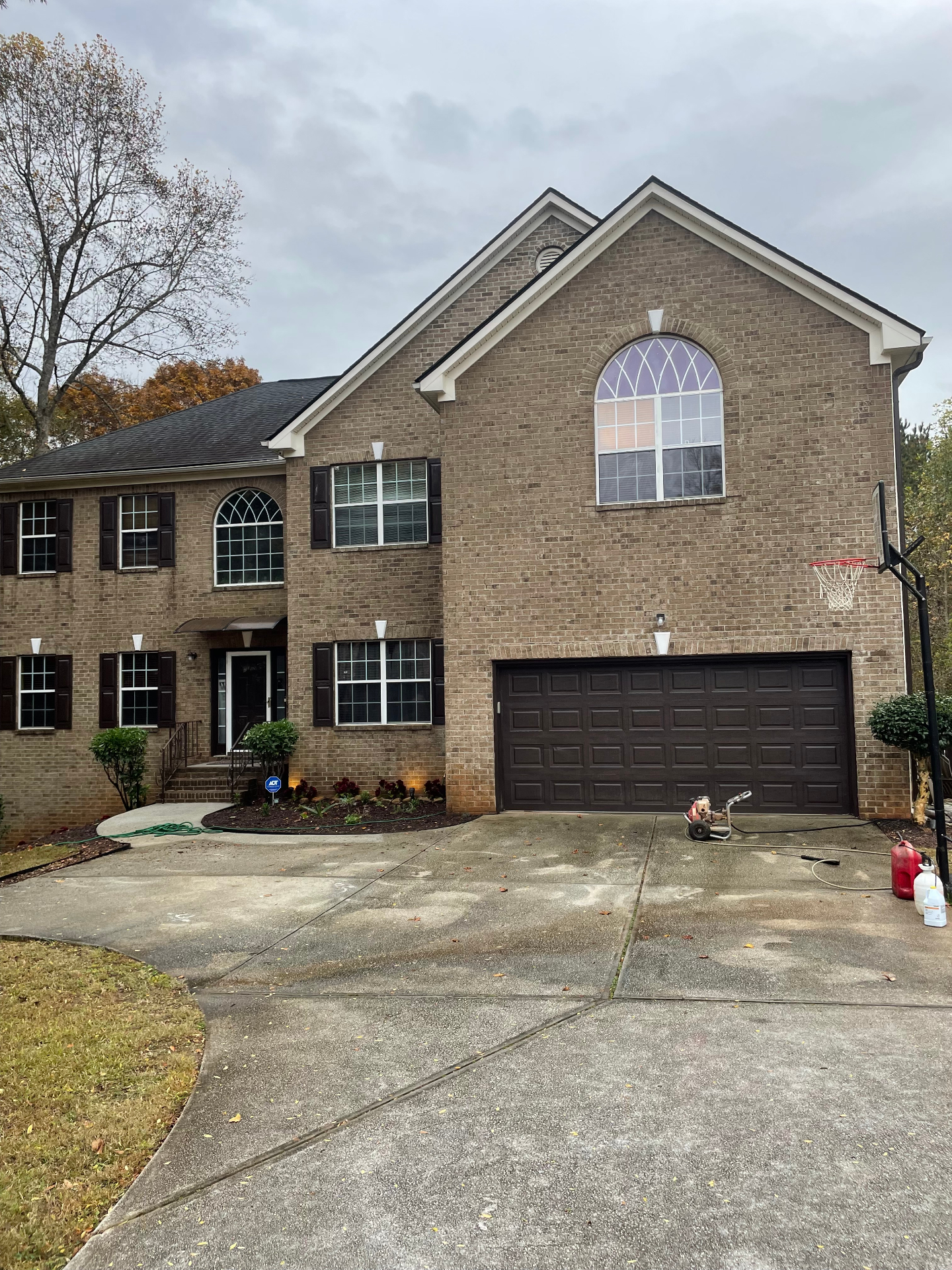 Two-story brick home with dark shutters and garage door, driveway prepped with sprayer for exterior wash