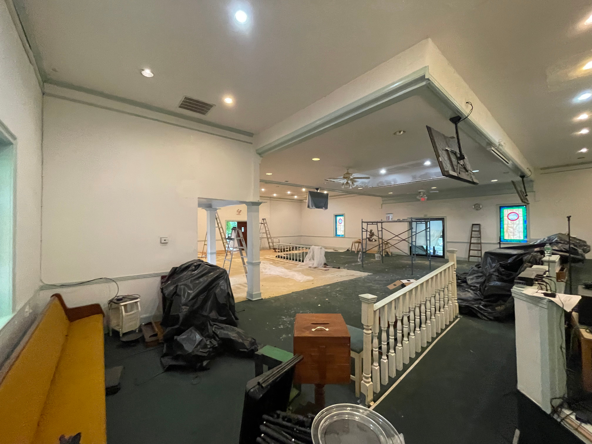 Church sanctuary mid-renovation with stained glass windows, drop cloths, and scaffolding in place