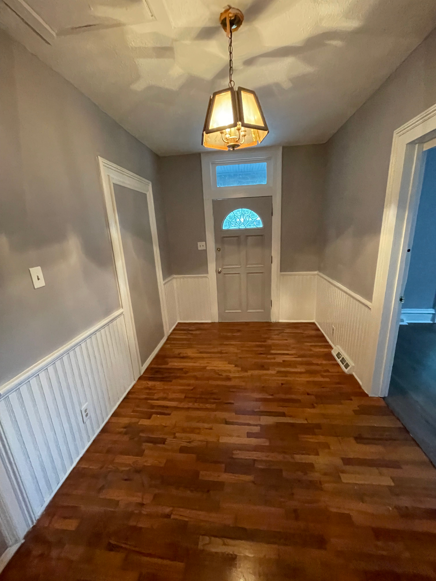 Refinished hardwood entryway with wainscoting and pendant light