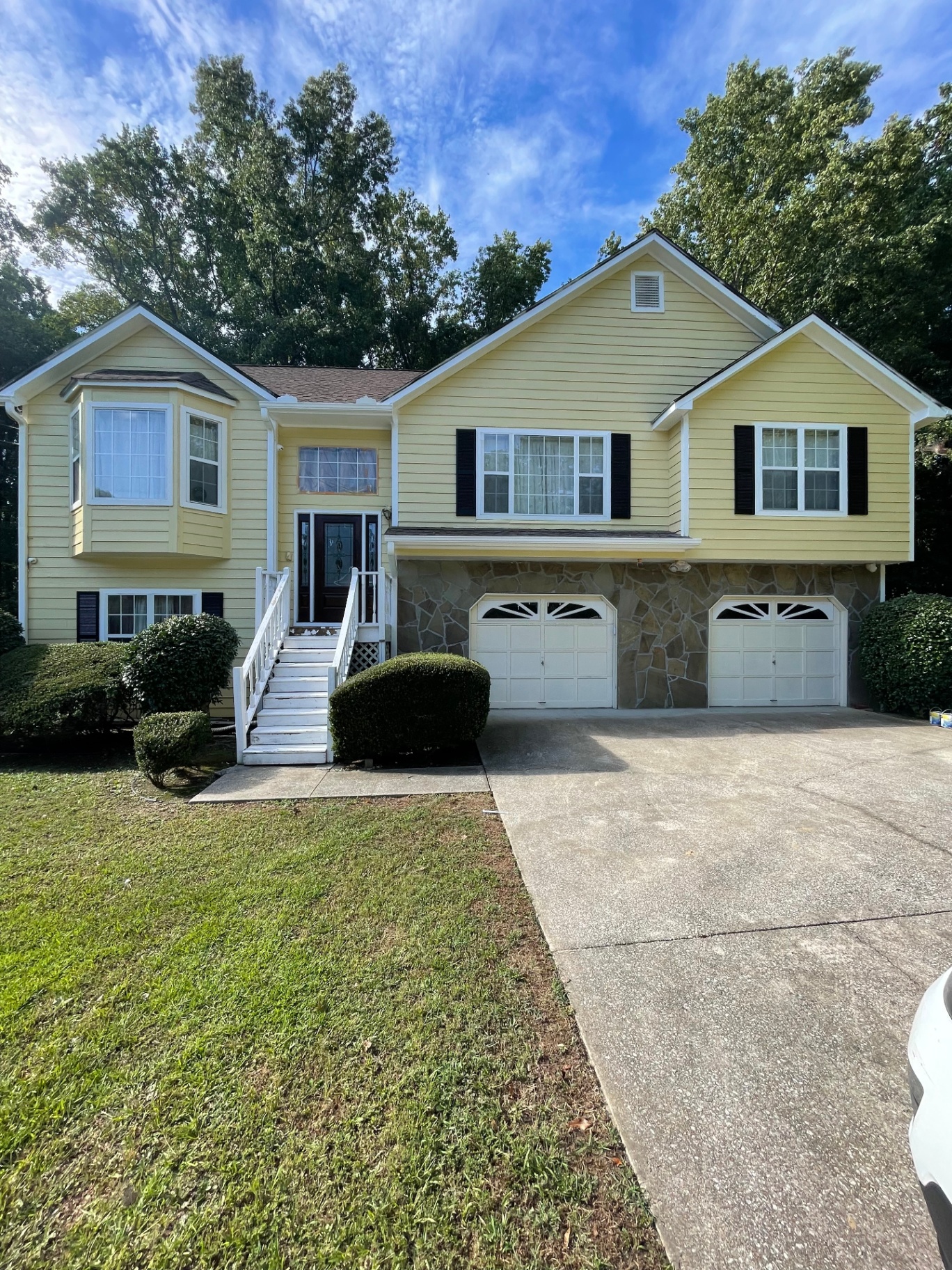 Full front exterior view of split-level yellow home with stone accents
