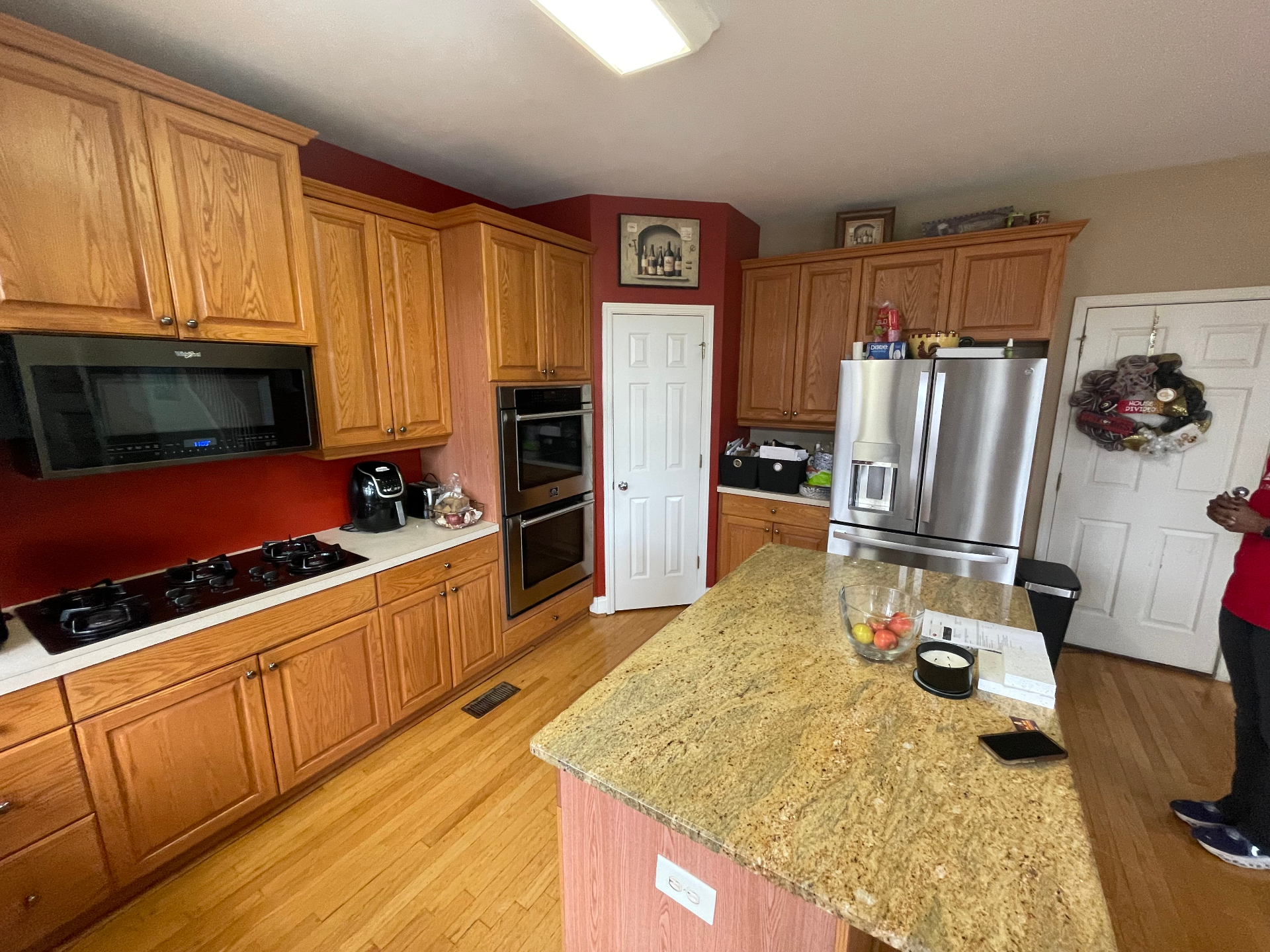 Kitchen with oak cabinets, red walls, double wall oven, and granite island before remodel