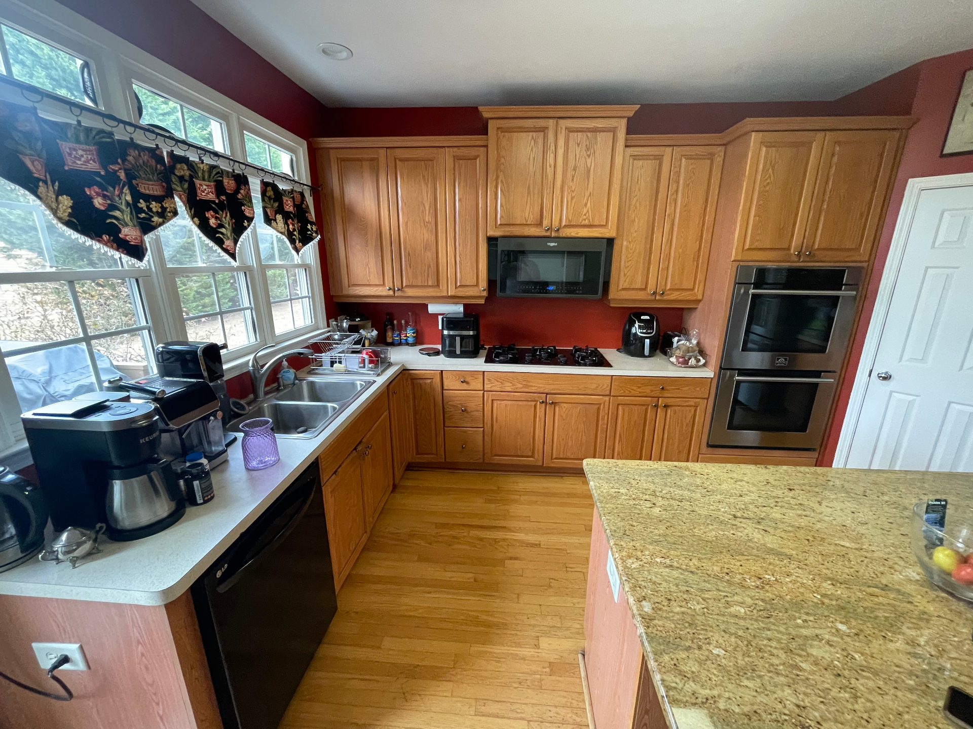 Wide view of oak cabinet kitchen with red walls and bay window before remodel