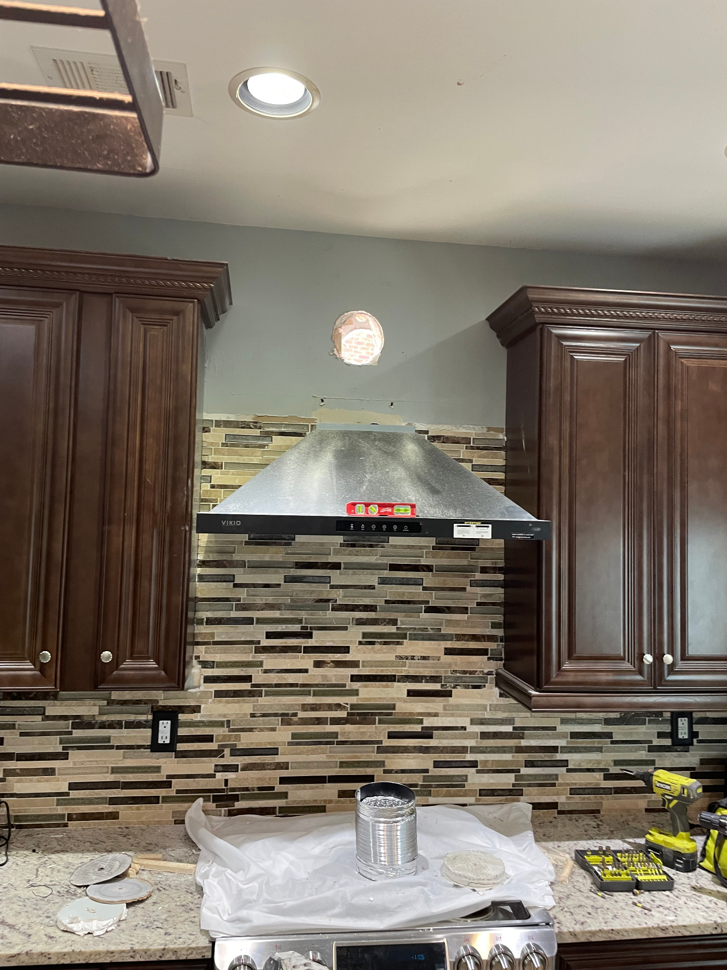 Stainless range hood installed between dark wood cabinets over a tile backsplash