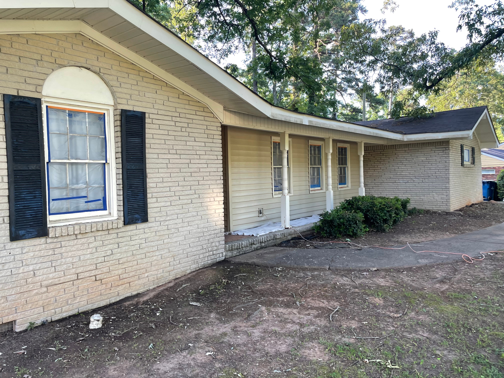 Single-story ranch home exterior masked and prepped for painting with shutters removed