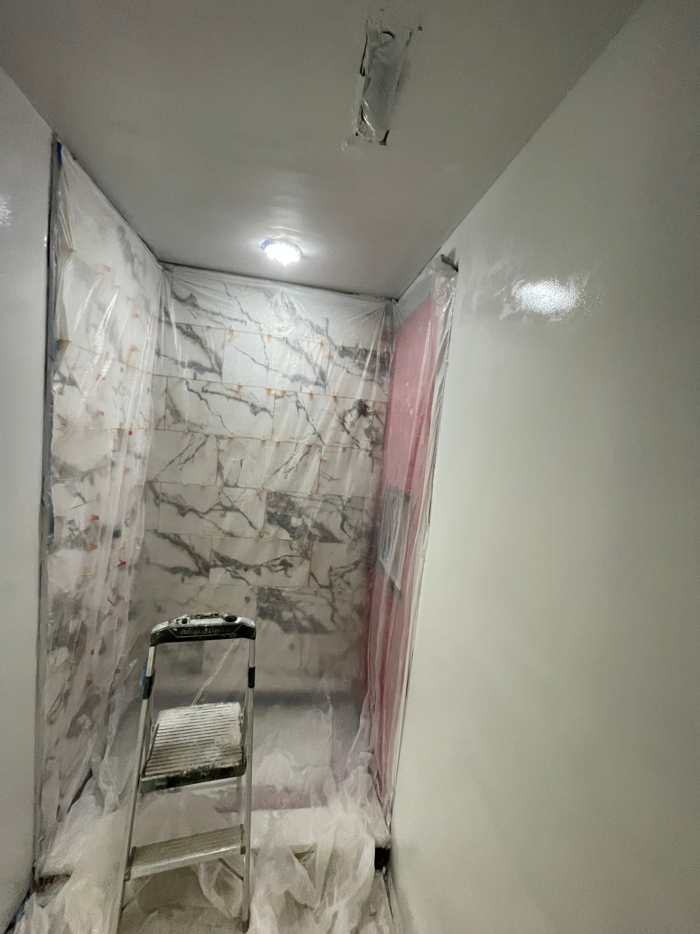 Marble-tiled shower masked off with plastic during bathroom paint prep