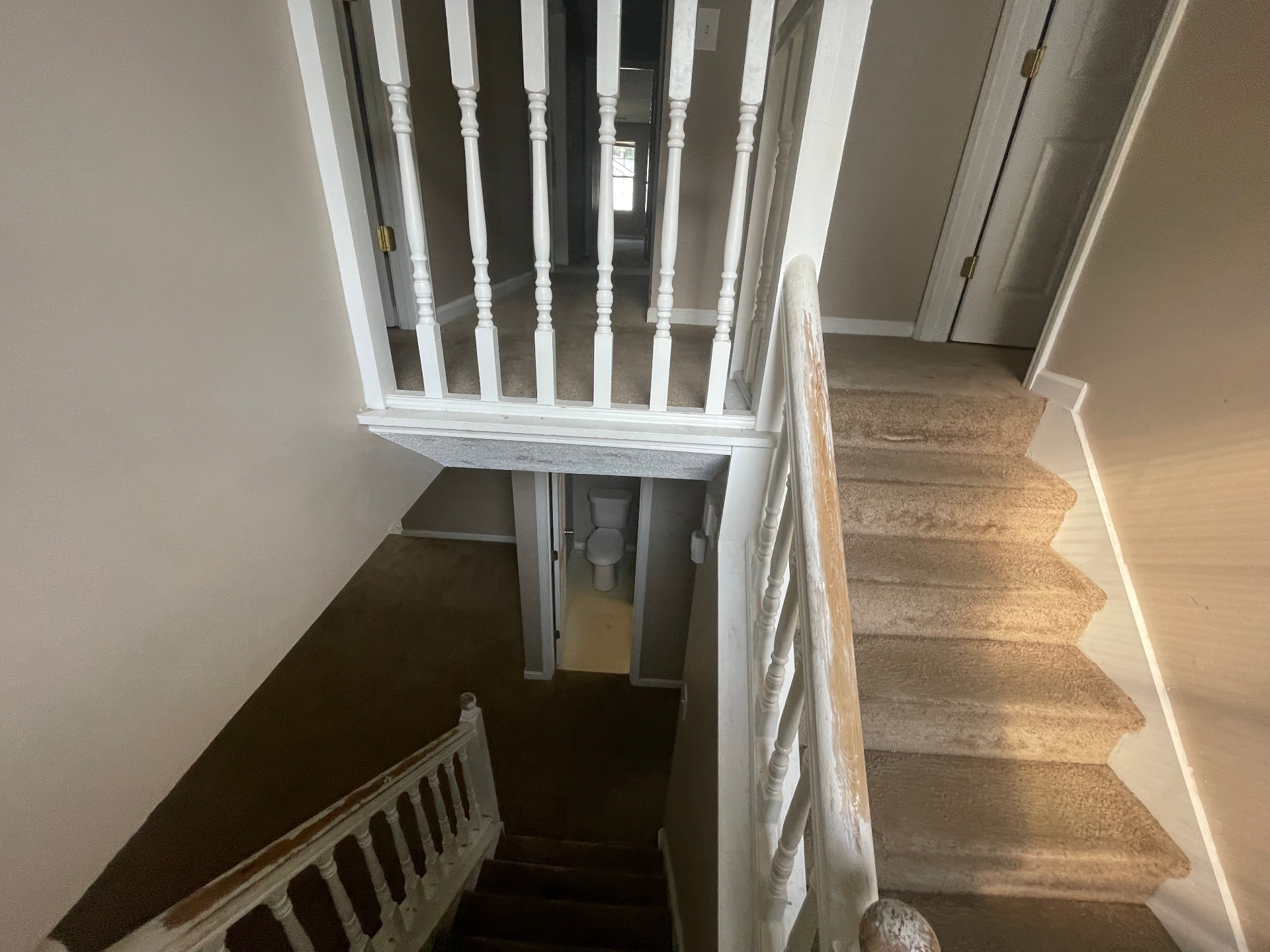 Interior stair landing with white balusters, worn handrail, and carpeted steps during repaint preparation