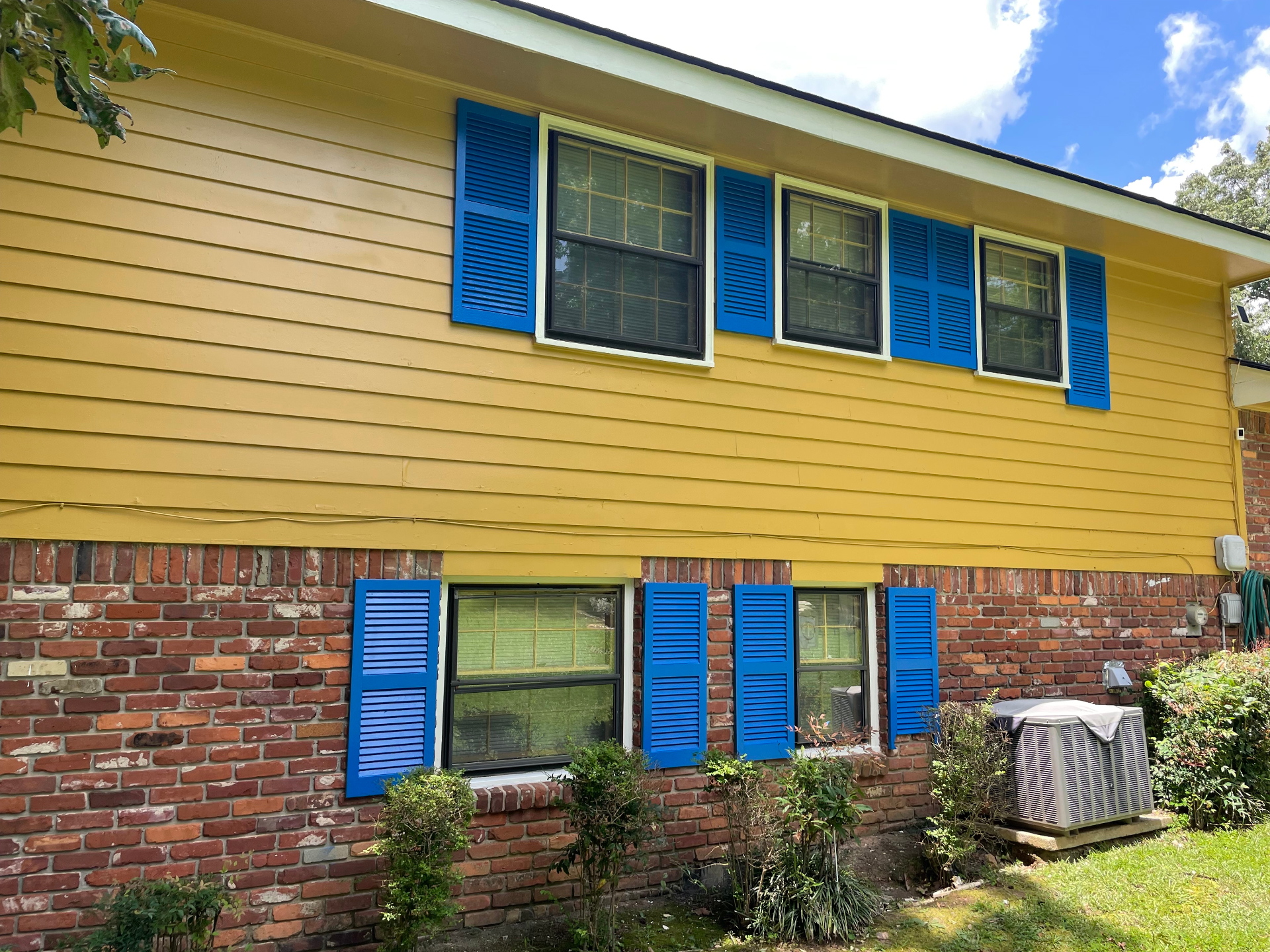 Yellow home exterior with bright blue shutters after a full repaint by RJM Contracting
